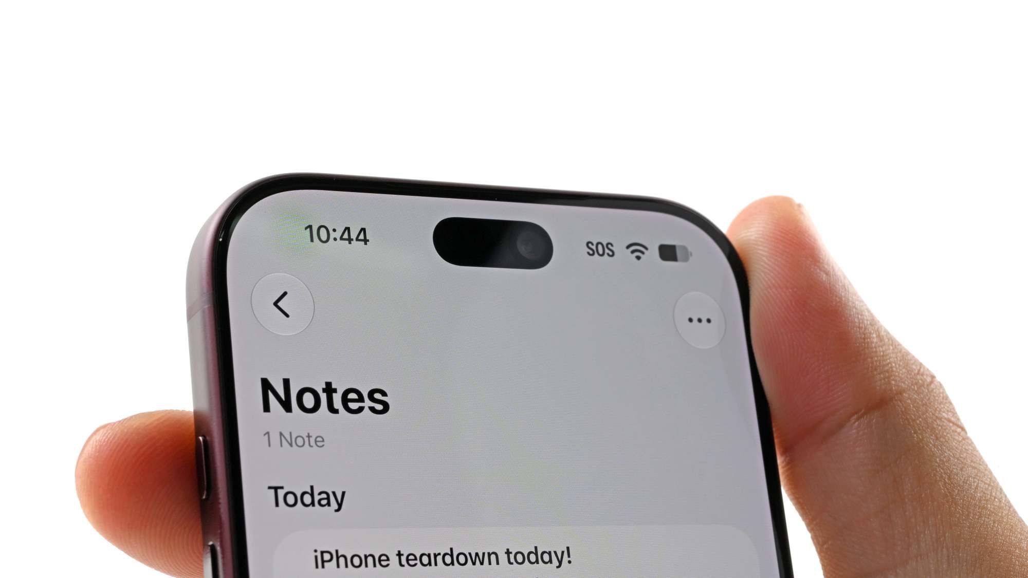 iFixit teardown photo: an iPhone 18 Pro in a hand, display on — the hidden sensor region is barely visible to the naked eye
